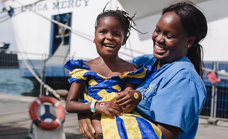 Une bénévole porte une patiente en chirurgie de Mercy Ships